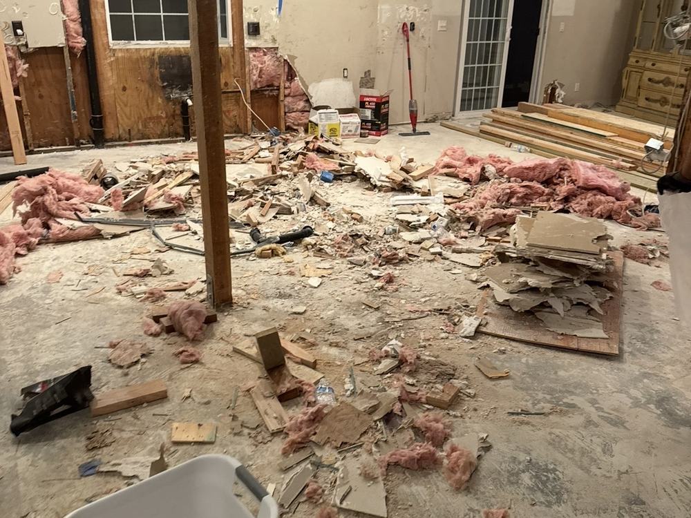 Gutted kitchen with drywall, insulation and lumber scraps across the floor before removal
