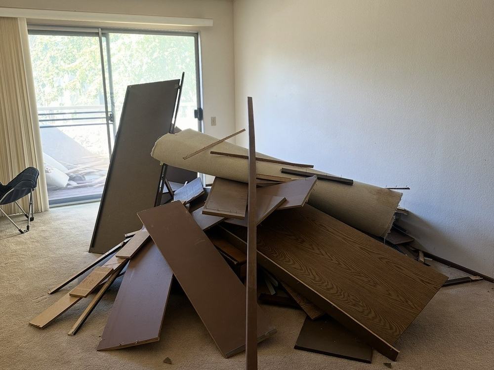 Living room with a pile of cabinet doors, shelving and rolled carpet before removal